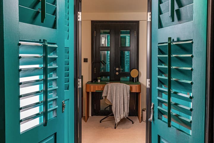 Interior view looking from the terrace toward the desk area, framed by vibrant teal louvered doors opening to a double black glass door.