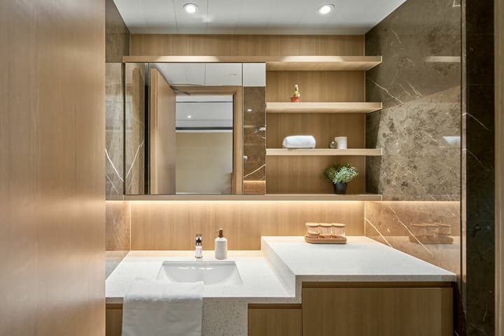 Elegant bathroom with wood cabinetry, marble wall tiles, and backlit shelving in a modern studio apartment at Weave Studios – Kai Tak.