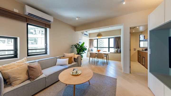 Contemporary open-concept living area with a grey sofa, circular coffee table, and a dining space with a built-in window seat and large windows.