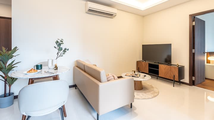 Bright living room featuring a tan sofa, round marble coffee table, wall-mounted TV cabinet, and a small dining table near a doorway.