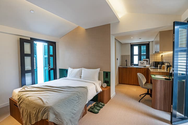 Open-concept studio apartment (Garden Suite) featuring a queen bed with storage, an integrated kitchenette with a desk, and double doors opening to a terrace.