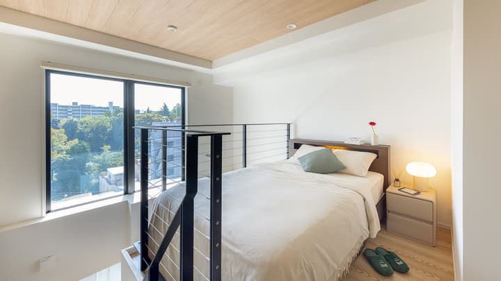 View of the loft bedroom level with a wooden ceiling, a double bed, and a black railing overlooking a large window with a view of greenery outside.